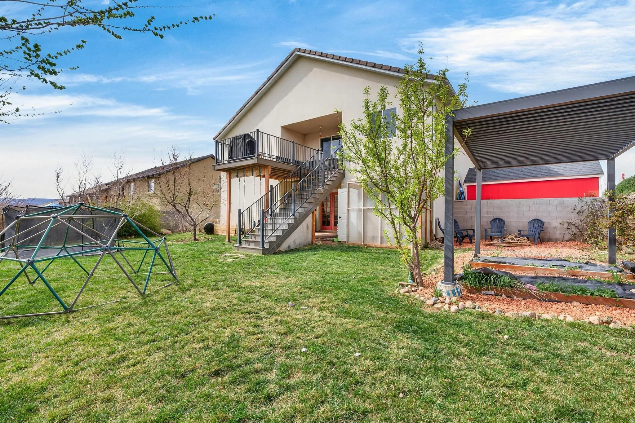Spacious backyard with a balcony, exterior staircase, and a pergola-covered patio area featuring raised garden beds