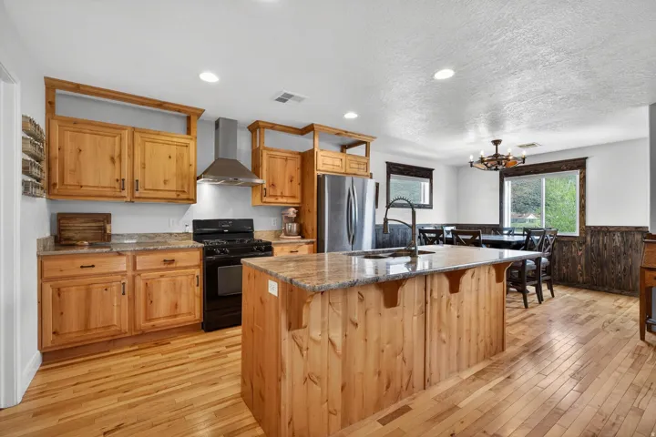 Open-concept kitchen featuring light wood-finish cabinetry, granite countertops, stainless steel appliances, and wood-finish flooring