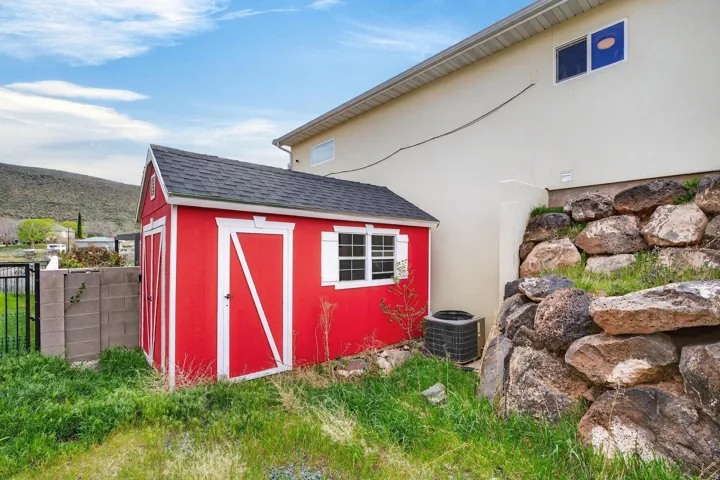 Red storage shed with white trim and a shingled roof, featuring a single window with white shutters and a double barn door entry