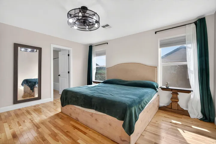 Bedroom featuring wood-finish flooring, a ceiling fan with integrated lighting, and two windows allowing for natural illumination
