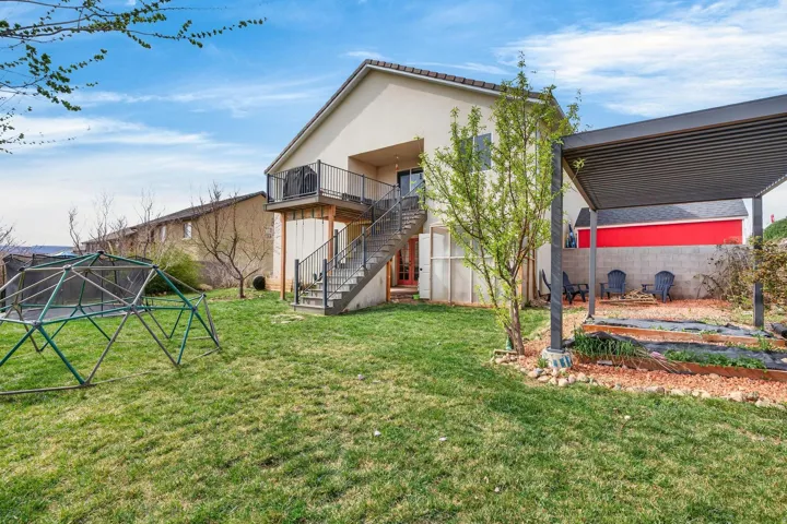 Spacious backyard with a balcony, exterior staircase, and a pergola-covered patio area featuring raised garden beds