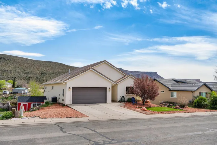 Single-story stucco exterior featuring a two-car garage, concrete driveway, and a red storage shed