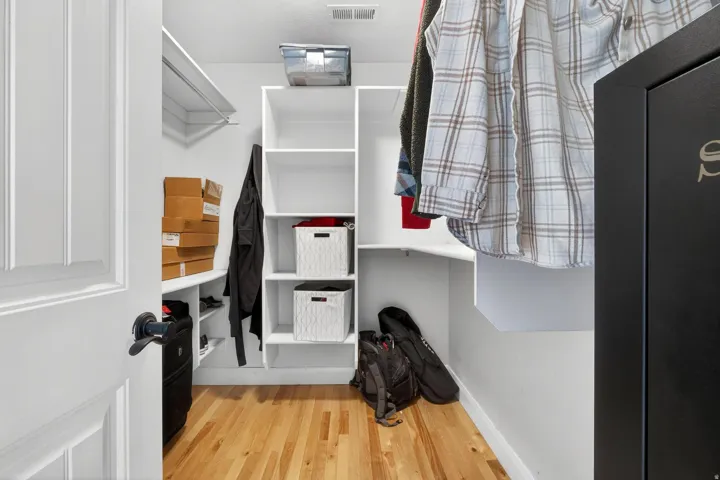 Walk-in closet featuring wood-finish flooring, white built-in shelving, white clothes hanging rods, and a white paneled door with matte black hardware