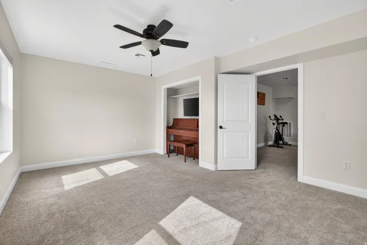 Spacious interior room featuring light gray carpeting, neutral wall paint, a ceiling fan, and white trim