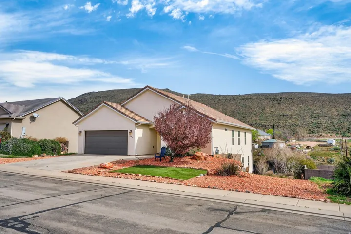 Contemporary stucco exterior featuring a two-car garage, pitched tile roof, and a low-maintenance landscape design with red rock and green lawn