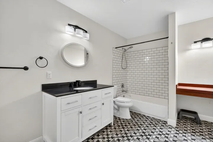 Bathroom featuring a white vanity with a black countertop, decorative floor tiling, subway tile shower surround, and contemporary black fixtures