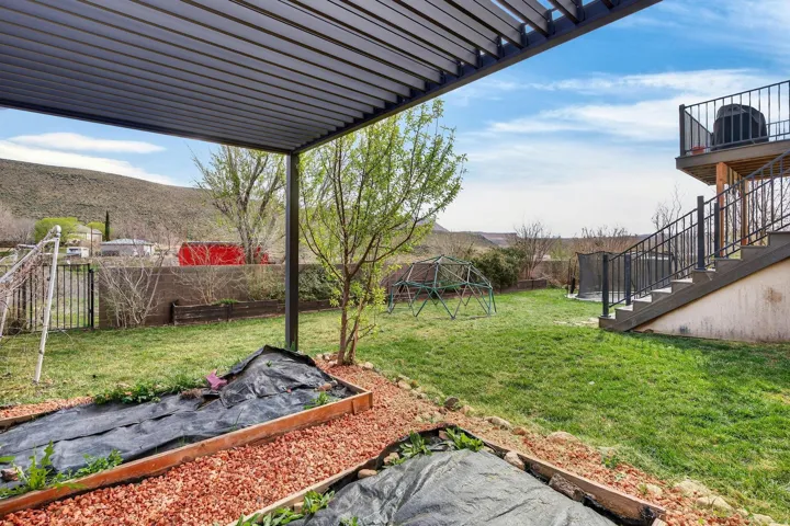 Expansive backyard featuring a covered patio, terraced landscaping with raised garden beds, a multi-level deck with stairs, and a mountain backdrop