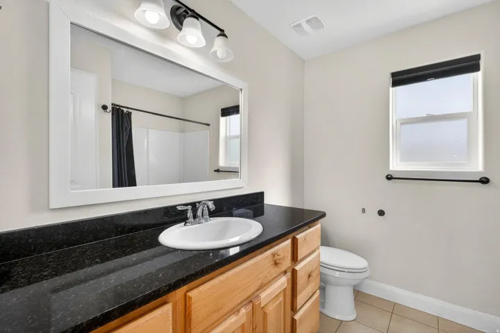 Bathroom vanity featuring a dark countertop with an integrated white sink, wood-finish cabinetry, and a large framed mirror