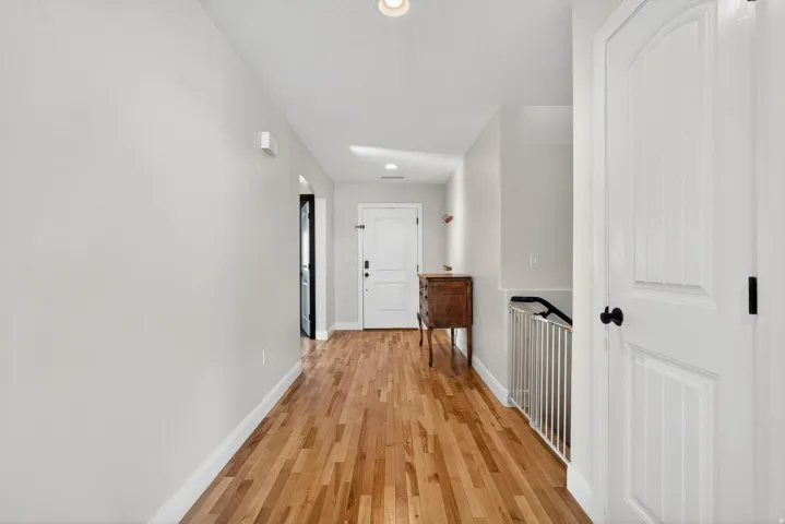 Bright hallway featuring wood-finish flooring, white baseboards, and a paneled interior door with matte black hardware
