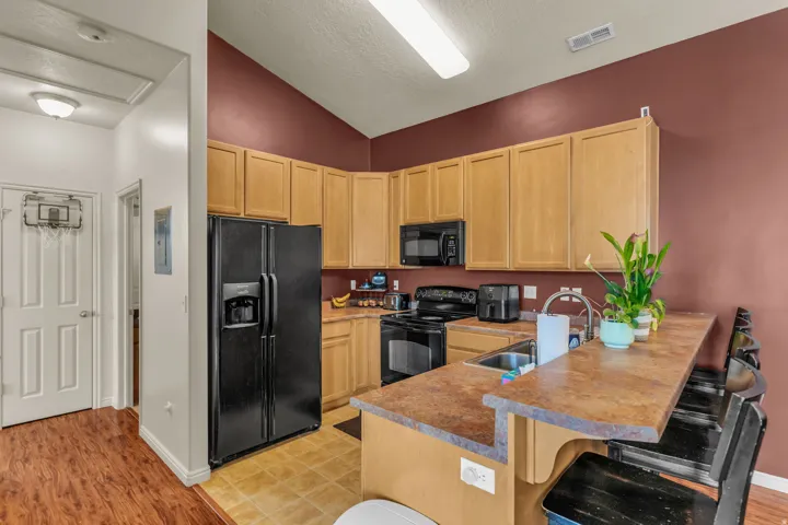 Kitchen featuring wood-finish cabinetry, black appliances, a double basin sink, and a breakfast bar with seating