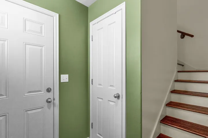 Staircase with wood-finish treads and a dark wood handrail, complemented by a white paneled door and green accent wall