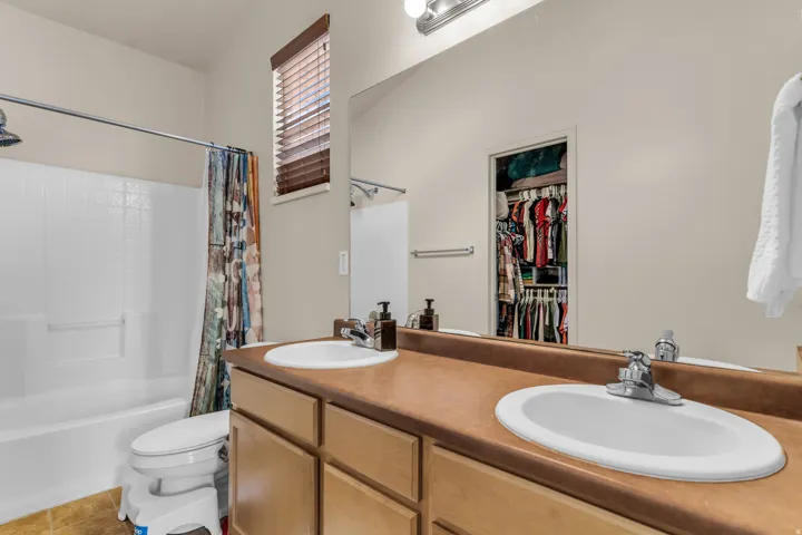 Bathroom featuring a double vanity with wood-finish cabinetry and integrated sinks, a shower-tub combination, and a high window with wood blinds