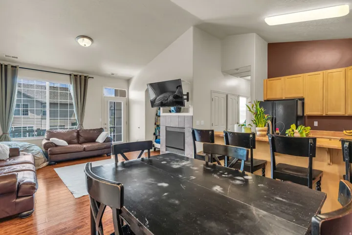 Open-concept living space featuring wood-finish flooring, a fireplace with a tiled surround, a kitchen with wood cabinetry and black appliances, a dining area, and a glass-paneled exterior door