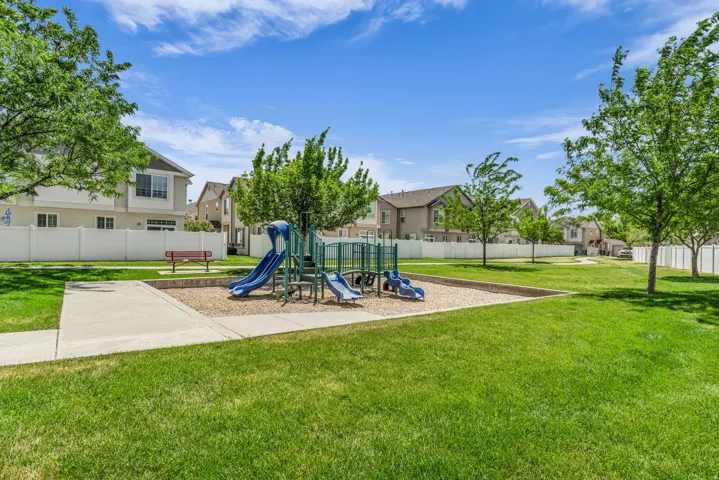 Community green space featuring a playground with slides and climbing structures, a bench, and a concrete pathway