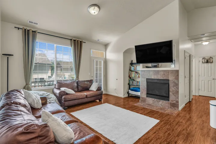 Living area featuring wood-finish flooring, a large window with blinds, and a tiled fireplace