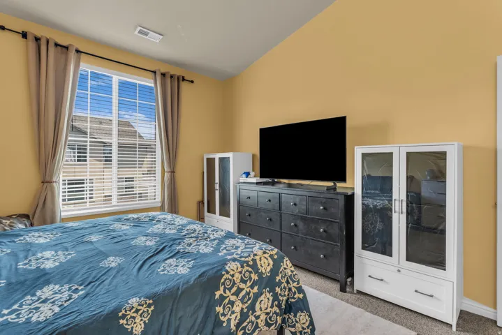 Vaulted ceiling bedroom featuring a large window with blinds, carpet flooring, and warm wall paint