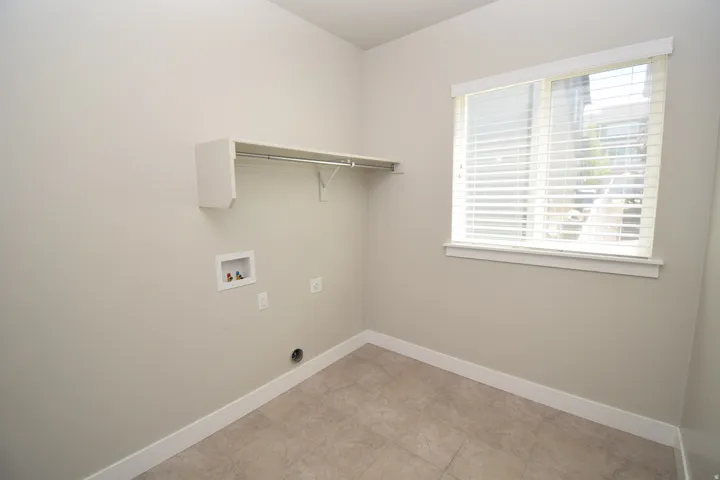 Dedicated laundry area featuring a built-in hanging rod, overhead shelving, and a prominent window with horizontal blinds
