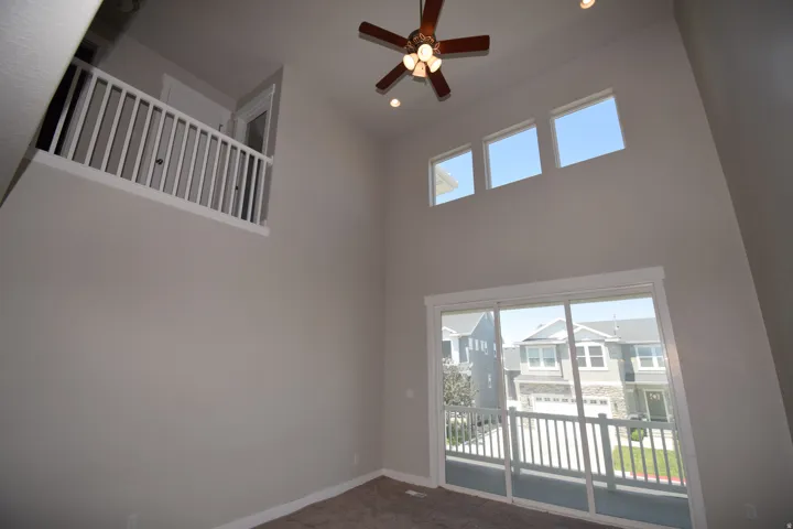 Vaulted ceiling featuring a wood-finish ceiling fan with integrated lighting, three upper transom windows, and a sliding glass door leading to a balcony with white railing