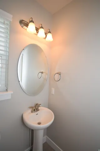 Pedestal sink with brushed nickel faucet, oval wall mirror, and three-light vanity fixture