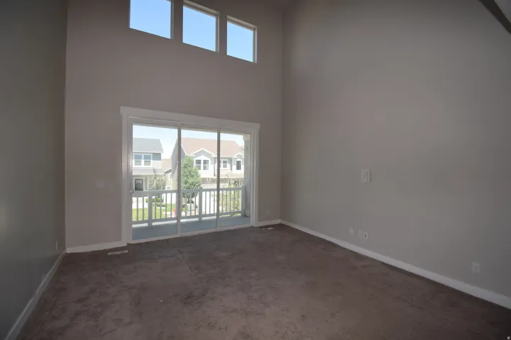 Spacious room featuring high ceilings, ample natural light from upper transom windows, a sliding glass door leading to an outdoor balcony, neutral wall tones, and plush carpeting