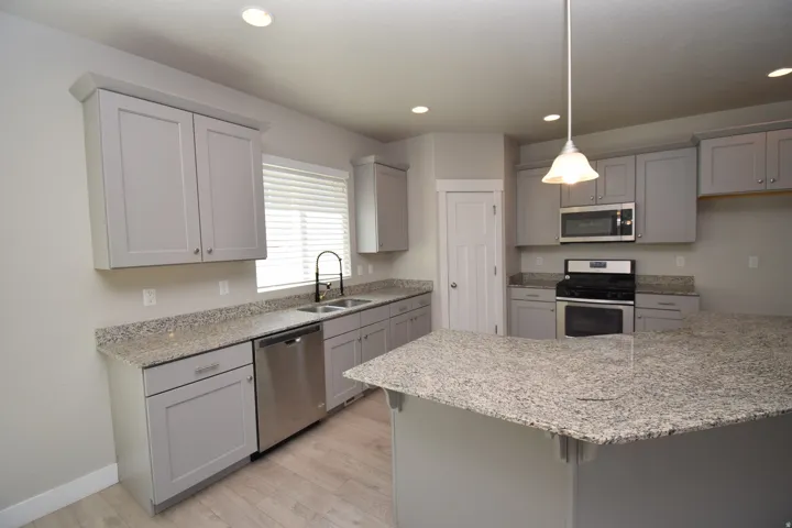 Kitchen featuring light gray cabinetry, speckled countertops, stainless steel appliances, and wood-finish flooring