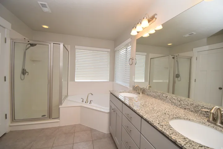 Bathroom featuring a glass-enclosed shower, corner soaking tub, dual vanity with granite countertop, and tile flooring