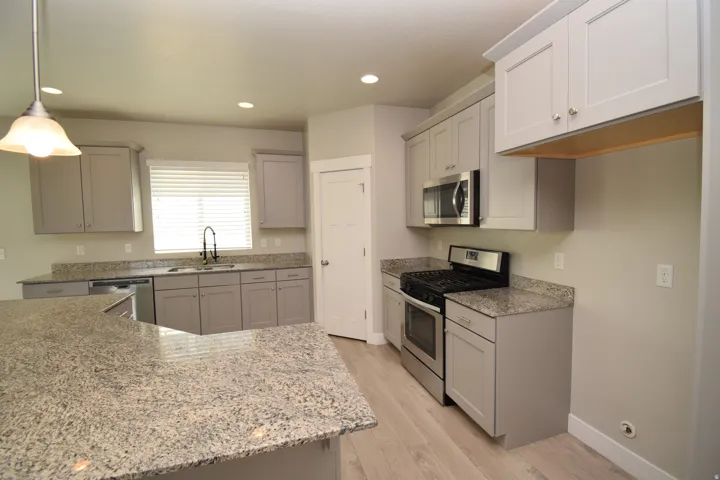 Kitchen featuring granite countertops, light gray cabinetry, stainless steel appliances, and wood-finish flooring
