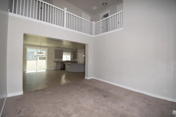 Two-story living area with an open concept design, featuring a carpeted floor, light gray wall tones, and white trim