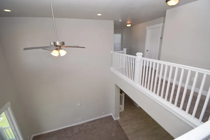 Two-story interior with white baluster railing, recessed lighting, and a ceiling fan with light fixture