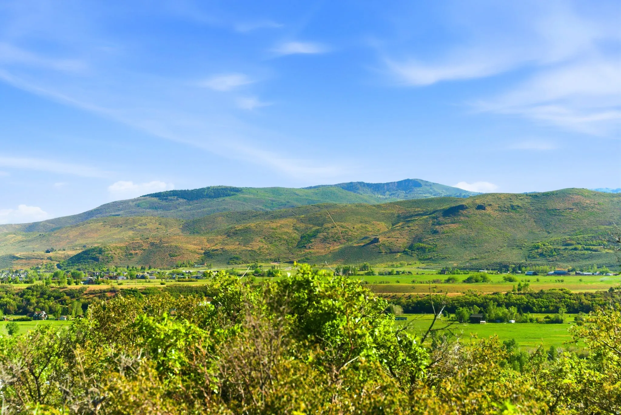 Expansive mountainous landscape featuring lush green foliage, rolling hills, and a bright blue sky