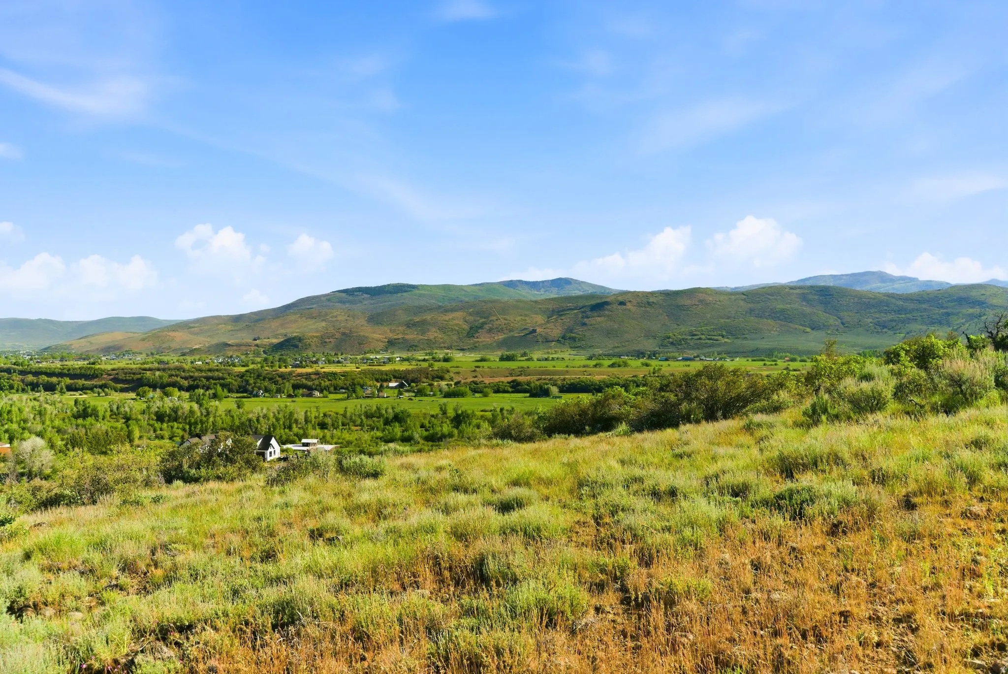 Expansive hillside property featuring distant mountainous terrain, a verdant valley, and a clear blue sky