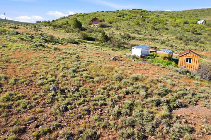 Expansive sloped terrain with scattered vegetation and a distant two-story residence