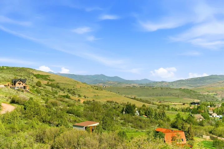 Expansive mountain landscape featuring a contemporary residence with a dark roof and light-colored siding, a detached shed with a brown roof, and verdant hillsides