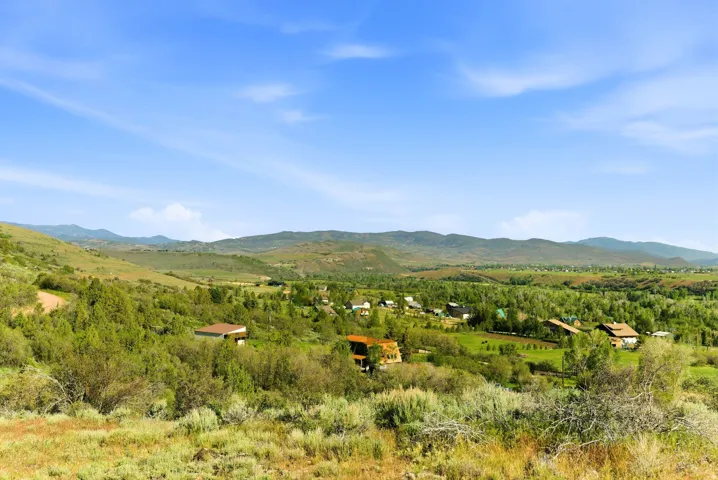 Expansive landscape featuring rolling hills, abundant green foliage, and distant mountain ranges