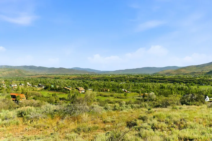 Expansive valley terrain featuring distant residential structures, abundant mature trees, and rolling hills
