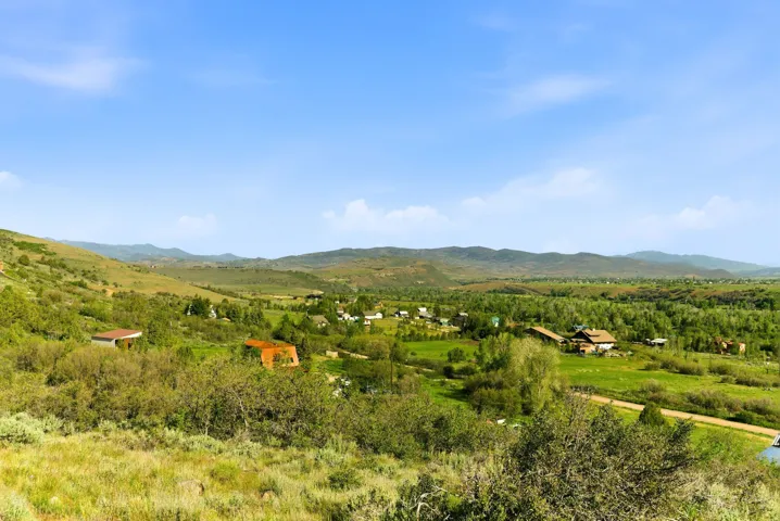Expansive rural landscape featuring rolling green hills and distant mountains under a clear blue sky