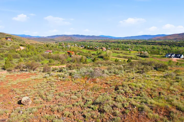 Expansive sloped terrain with natural vegetation, featuring distant mountain ranges and scattered residential structures