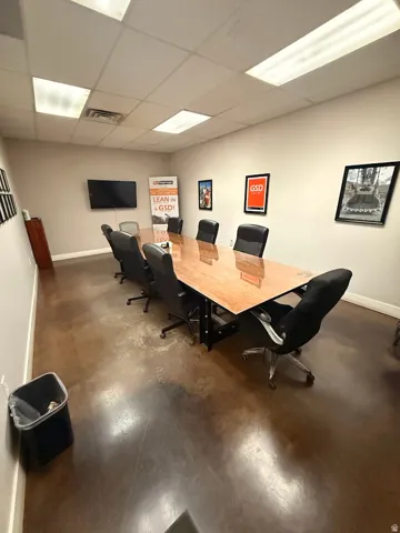 Conference room featuring a large wood-finish table with metal base, mounted flat-screen display, and exposed concrete flooring