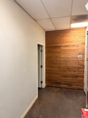 Entryway featuring a wood-panel accent wall, concrete flooring, and a drop ceiling with integrated lighting
