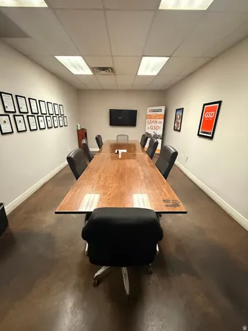 Conference room featuring a long wood-finish table with integrated power access, concrete-finish flooring, recessed lighting, and a wall-mounted display
