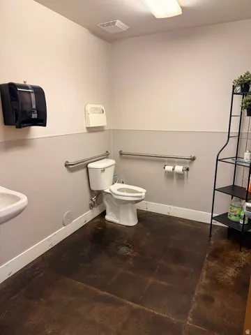 Restroom featuring a white toilet, wall-mounted sink, textured flooring, and a two-tone wall finish