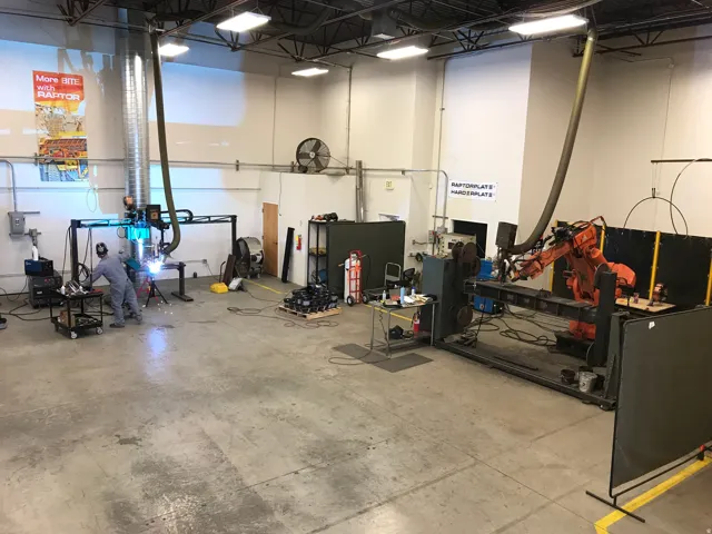 Industrial workspace featuring a concrete floor, high ceilings, exposed ductwork, and fluorescent lighting