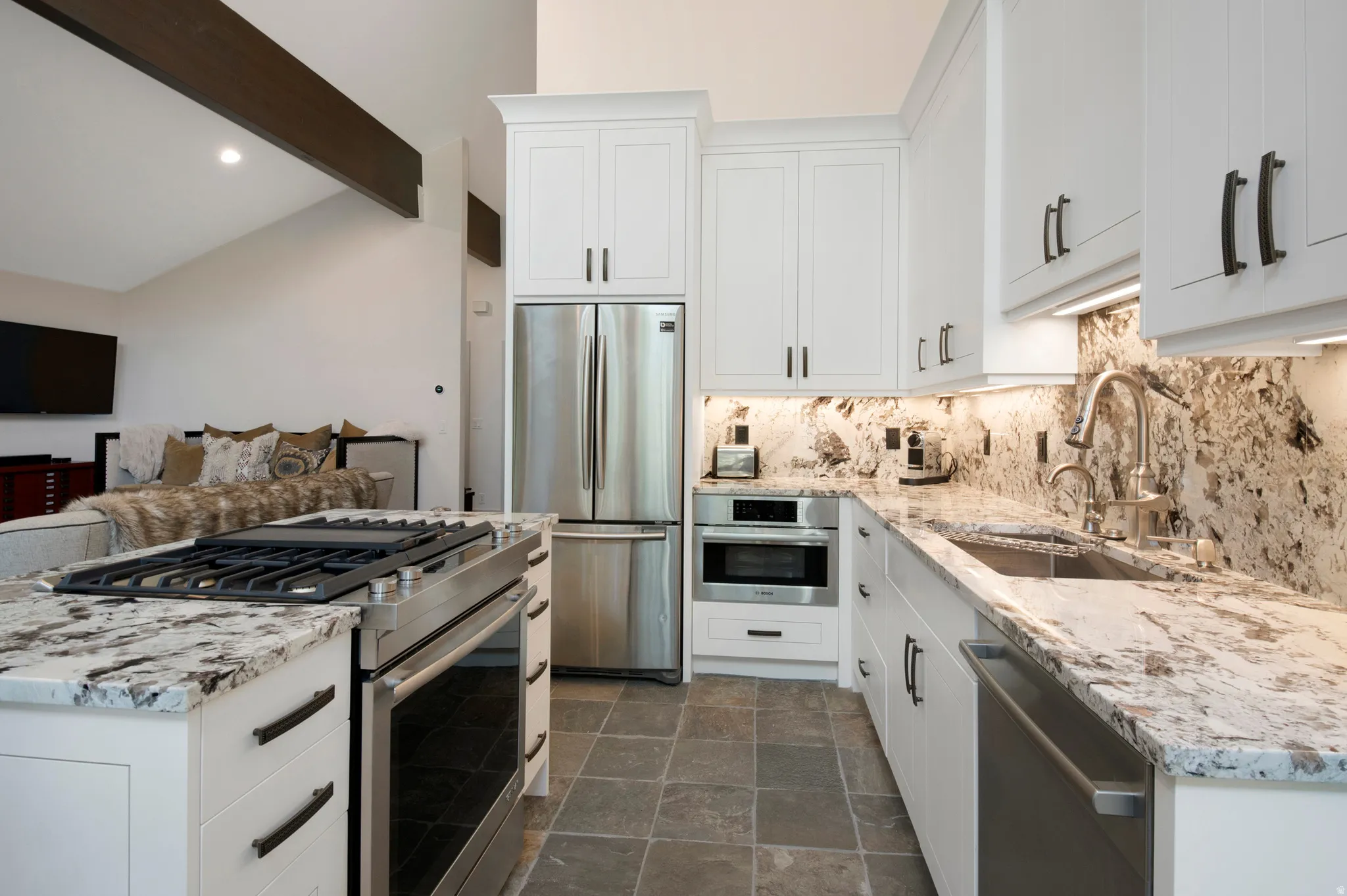 Gourmet kitchen featuring white shaker cabinetry, stainless steel appliances, premium stone countertops, a coordinating stone backsplash, and slate-finish flooring