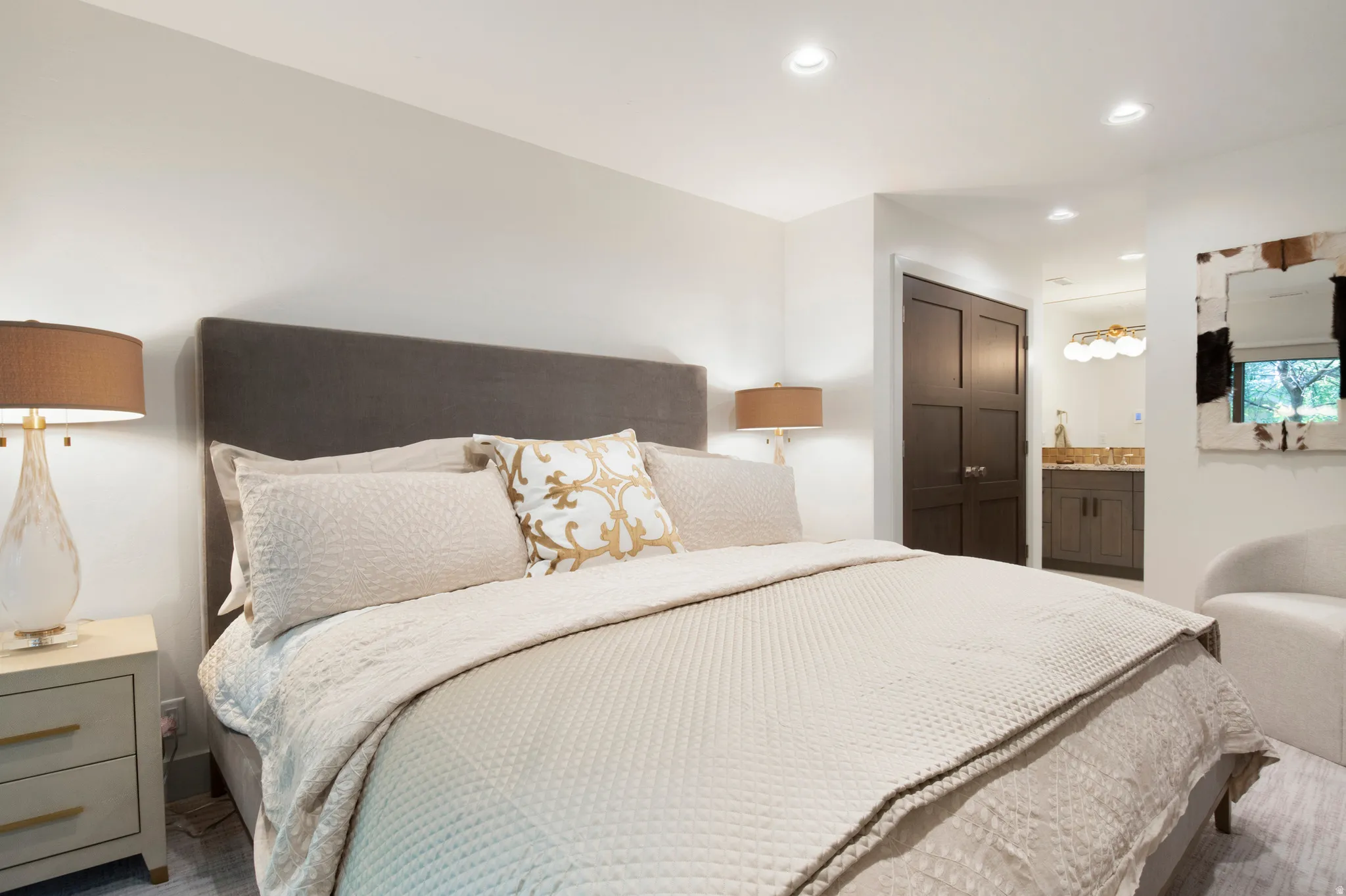 Recessed lighting illuminates this bedroom featuring a dark wood-finish paneled door, a bathroom vanity with a basin sink, and a multi-bulb vanity light fixture