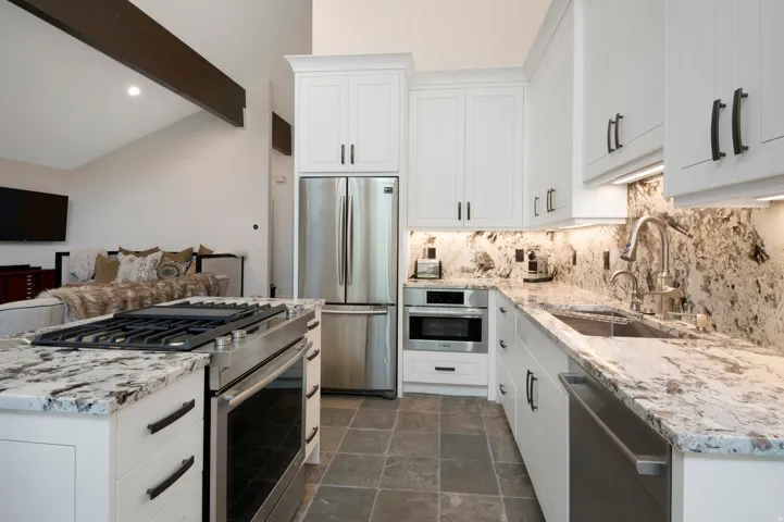 Gourmet kitchen featuring white shaker cabinetry, stainless steel appliances, premium stone countertops, a coordinating stone backsplash, and slate-finish flooring