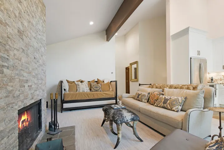 Stone-clad fireplace with slate hearth, vaulted ceilings, and exposed wood beam