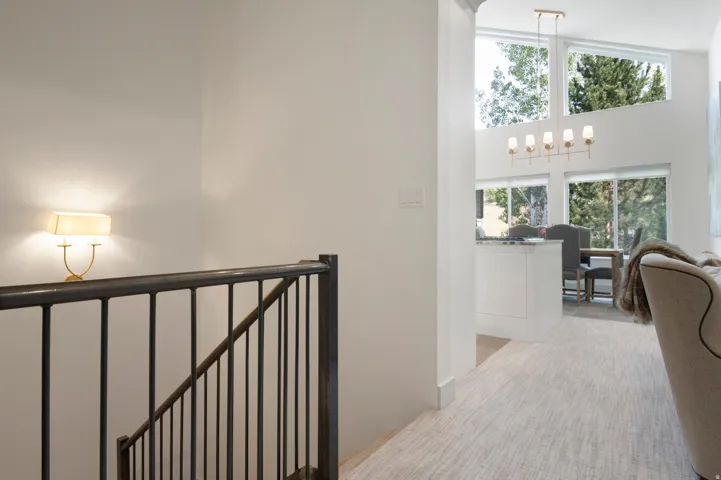 Open-concept living space with vaulted ceilings, large picture windows, a contemporary chandelier, and a stairway featuring a wrought iron railing with a wall sconce