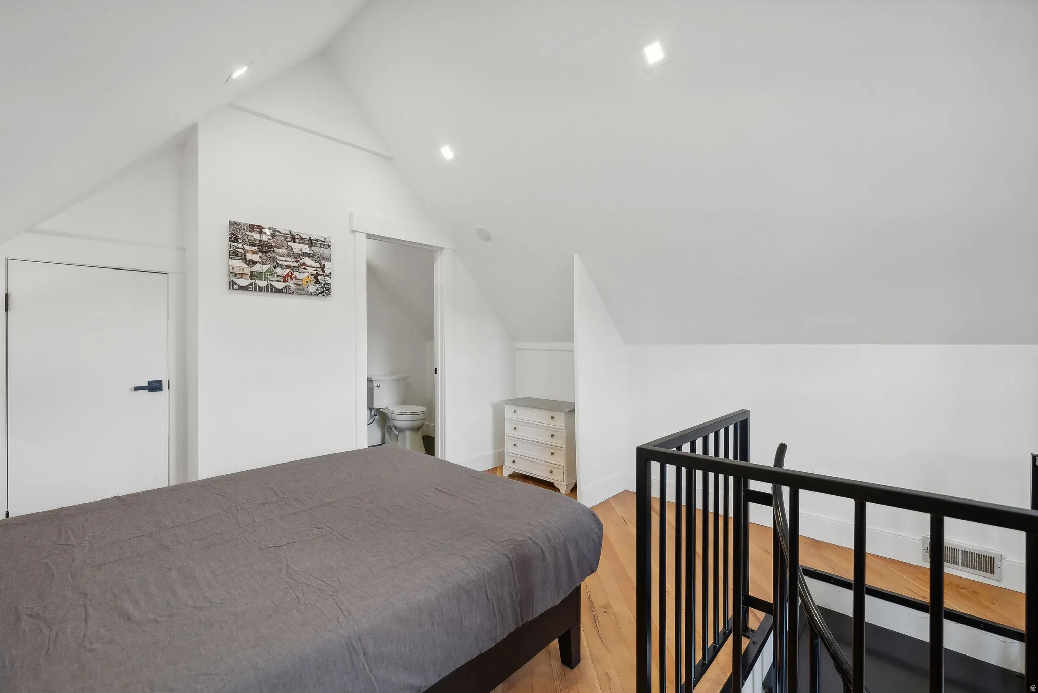 Attic bedroom featuring vaulted ceilings, light wood-finish flooring, recessed lighting, and a black metal railing