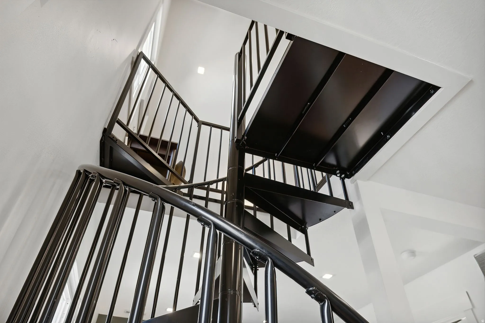 Spiral staircase featuring black metal construction, white wall finishes, recessed lighting, and a prominent window
