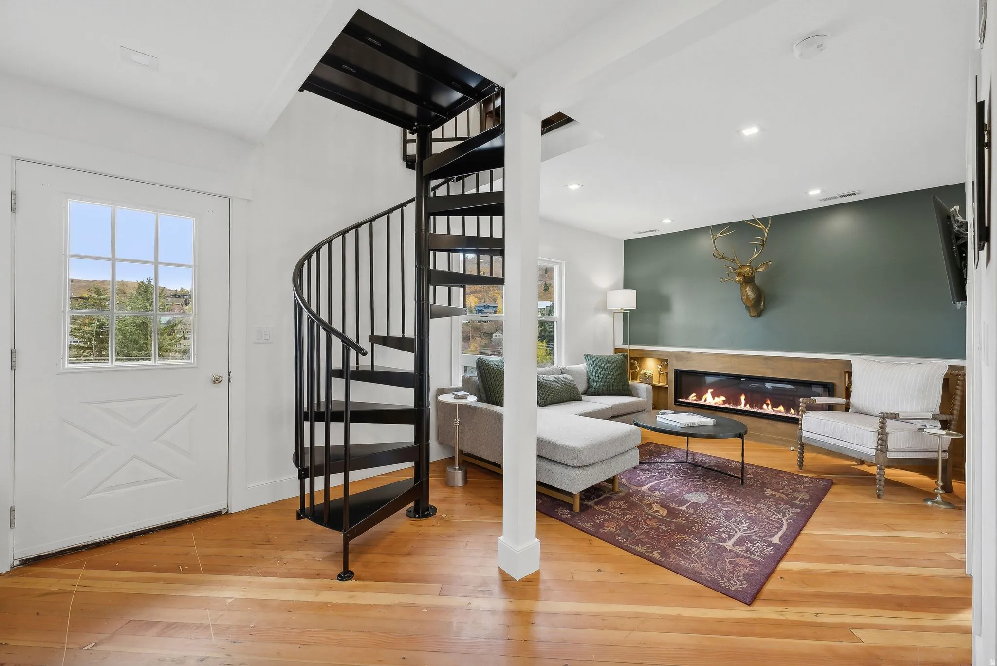 Hardwood flooring highlights an open living area featuring a sleek linear fireplace with a wood-finish mantel and a contrasting accent wall